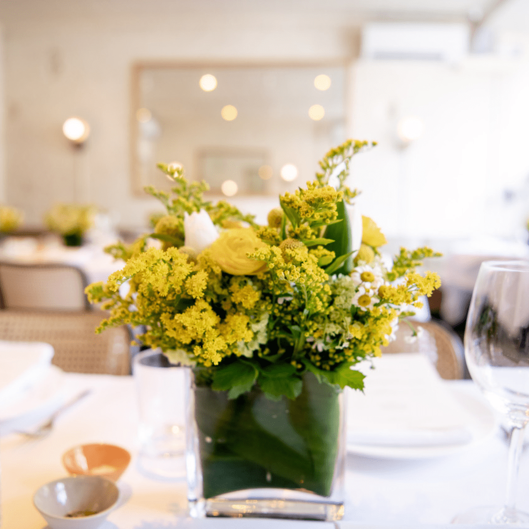 Small rectangular yellow centerpiece featuring seasonal flowers including Ranunculus