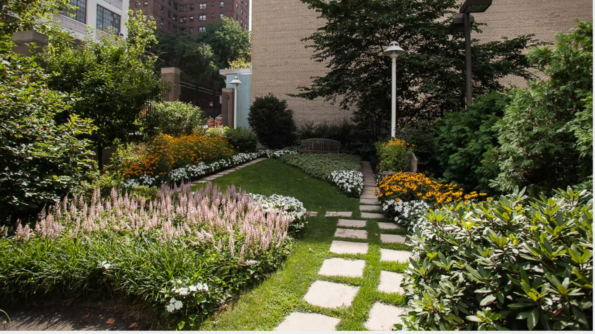 Lush commercial landscaping courtyard featuring colorful blooms including Impatiens, Astilbe, Black eyed Susies and evergreens. 