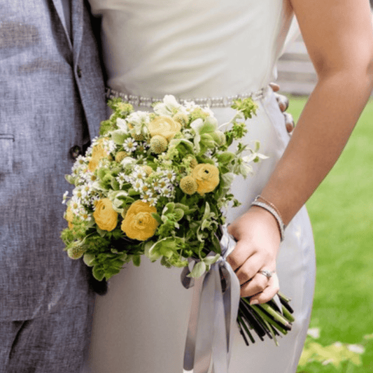 Small bridal bouquet featuring yellow, green and white flowers including Ranunculus and Chamomile